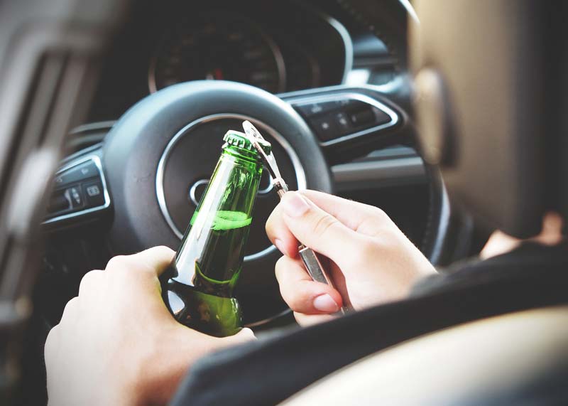 a man opening a beer bottle while driving in a car