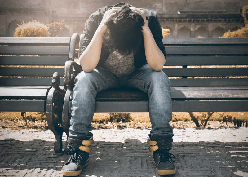 a young teenage boy sitting on a park bench with his hands over his head